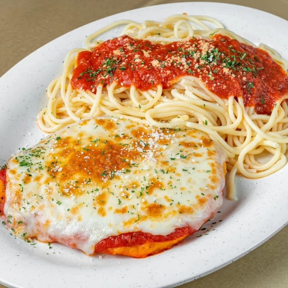 Chicken Parmesan with melted mozzarella and spaghetti with marinara sauce, garnished with parsley and cheese.