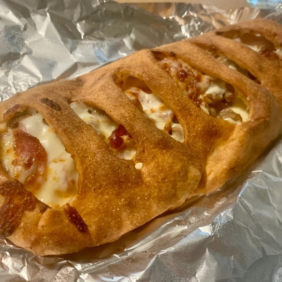 A golden-brown calzone with visible melted cheese and pepperoni, resting on aluminum foil.