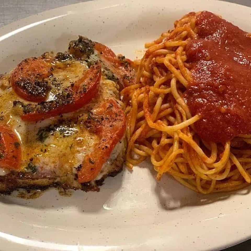 Chicken parmesan topped with tomatoes and herbs, served with a side of spaghetti and red sauce.